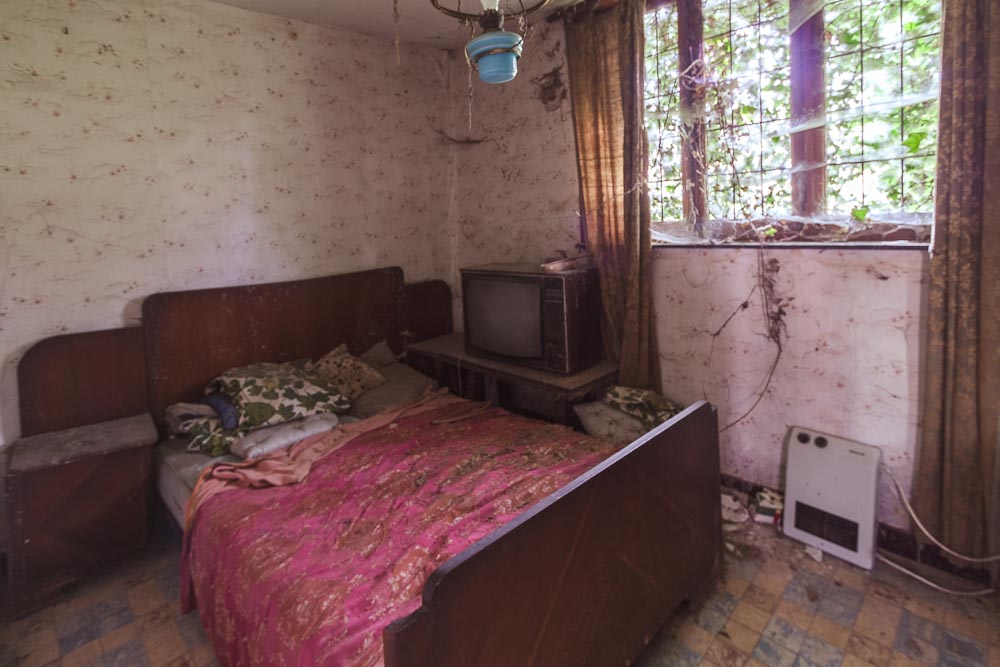 beeld van de slaapkamer van de urbex locatie ferme tapioca,
              een verlaten boerderij waar spinnenwebben tot het decor behoren